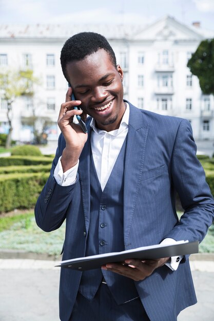 Un jeune homme d&#39;affaires africain en regardant presse-papiers parler sur téléphone mobile