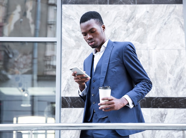 Un jeune homme d&#39;affaires africain tenant une tasse de café jetable à l&#39;aide de téléphone portable