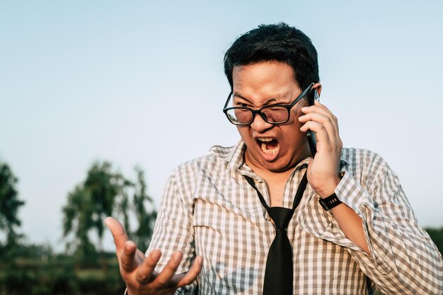 Jeune homme d'affaires asiatique drôle portant une chemise et une cravate avec un short et des lunettes avec un smartphone à la main criant un espace de copie de posture de manière folle et drôle