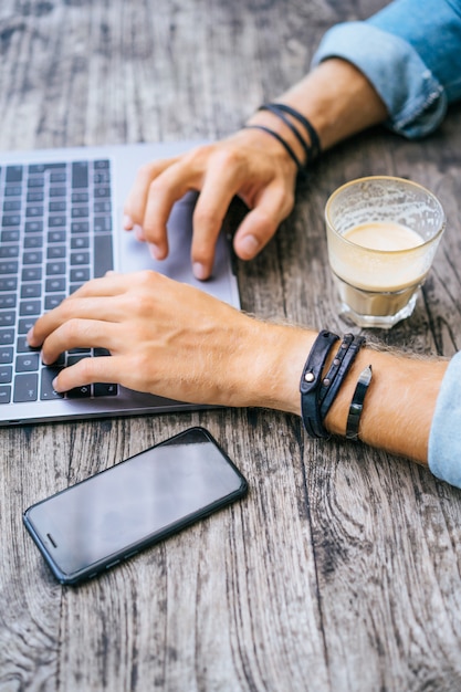 jeune homme d&#39;affaires attrayant dans un café travaille pour un ordinateur portable, boit du café.