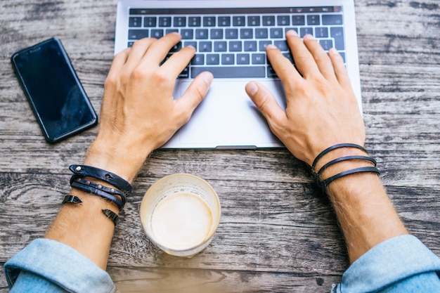 jeune homme d&#39;affaires attrayant dans un café travaille pour un ordinateur portable, boit du café.