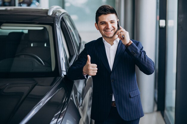 Jeune homme d'affaires beau dans une salle d'exposition de voiture choisir une voiture