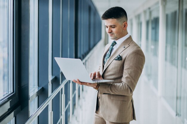 Jeune homme d'affaires beau debout avec un ordinateur portable au bureau