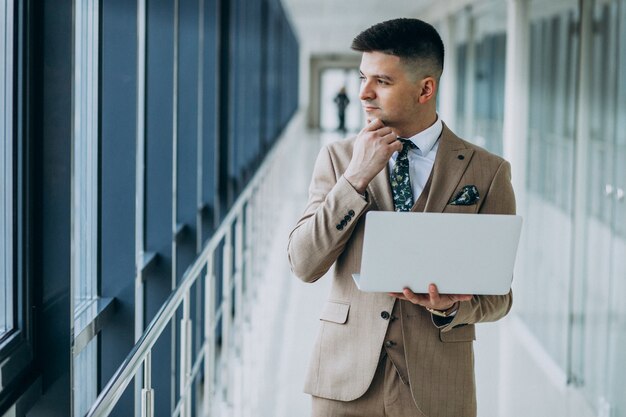 Jeune homme d'affaires beau debout avec un ordinateur portable au bureau