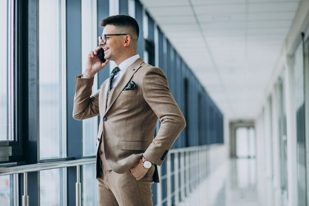 Jeune homme d'affaires beau debout avec téléphone au bureau