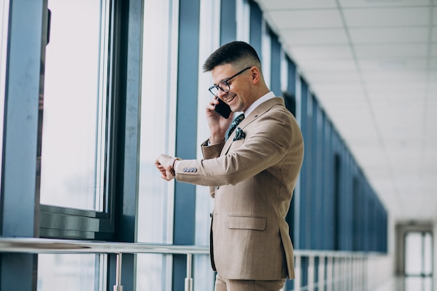 Jeune homme d'affaires beau debout avec téléphone au bureau