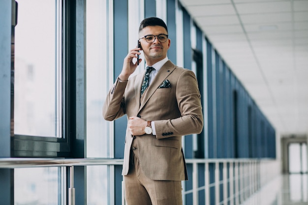 Jeune homme d'affaires beau debout avec téléphone au bureau