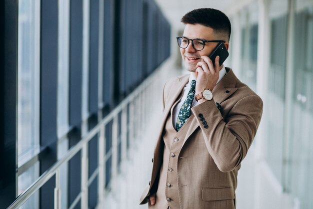 Jeune homme d'affaires beau debout avec téléphone au bureau