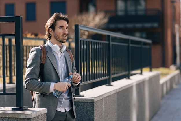 Jeune homme d'affaires avec une bouteille d'eau marchant dans la ville