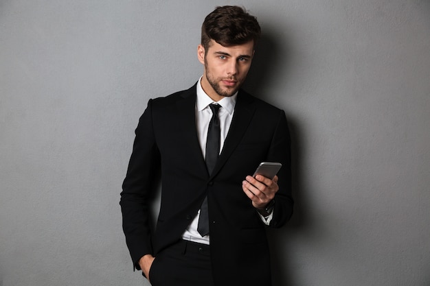 Jeune homme d'affaires confiant avec la main dans sa poche tenant un téléphone mobile,