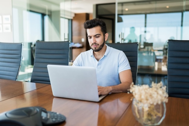 Photo gratuite jeune homme d'affaires dévoué travaillant sur un ordinateur portable au bureau dans la salle de réunion
