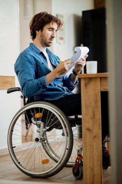 Jeune homme d'affaires en fauteuil roulant passant par la paperasse tout en travaillant à la maison.