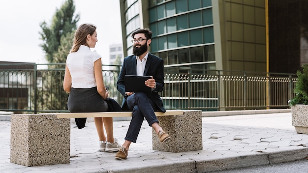 Jeune homme d'affaires et femme d'affaires assis sur un banc à l'extérieur de l'immeuble de bureaux