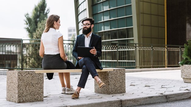 Jeune homme d&#39;affaires et femme d&#39;affaires assis sur un banc à l&#39;extérieur de l&#39;immeuble de bureaux