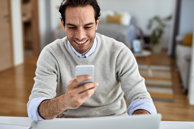 Jeune homme d'affaires heureux travaillant à la maison et messagerie texte sur téléphone mobile