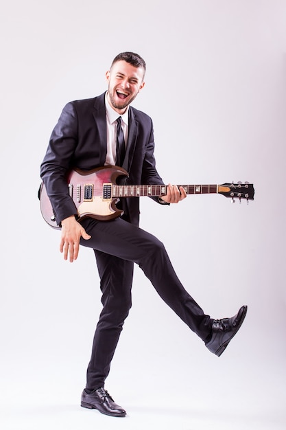 Jeune homme d'affaires jouant de la guitare isolé sur mur blanc