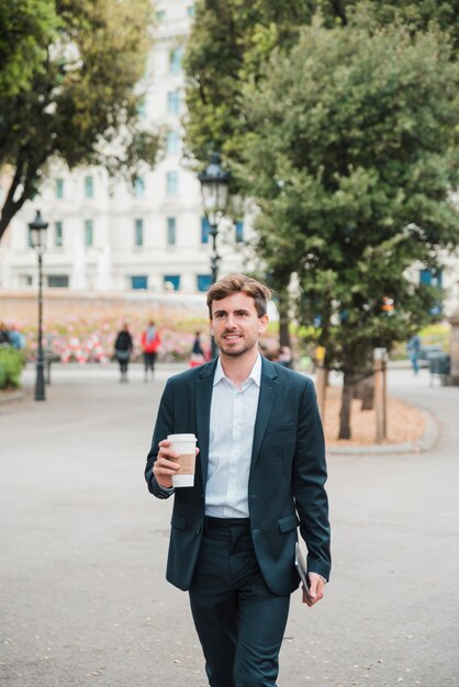 Jeune homme d&#39;affaires marchant avec tablette numérique et tasse de café sur la rue