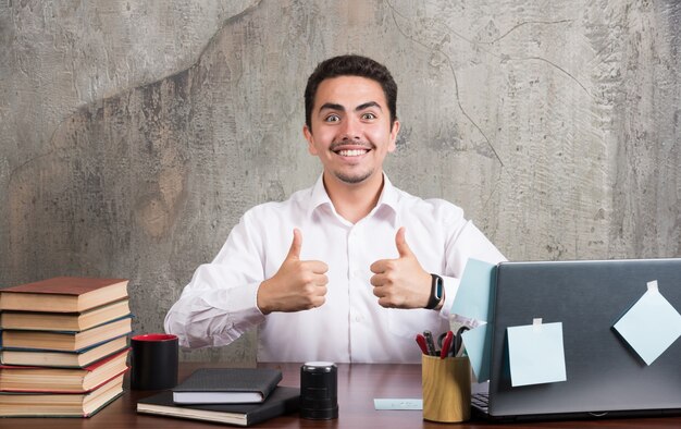 Jeune homme d'affaires montrant joyeusement les pouces vers le haut au bureau.