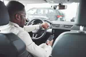 Photo gratuite jeune homme d'affaires noir teste une nouvelle voiture. homme afro-américain riche.