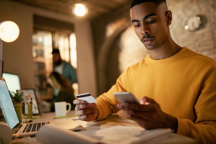 Photo gratuit jeune homme d'affaires noir utilisant une carte de crédit et un téléphone intelligent lors de ses achats en ligne au bureau