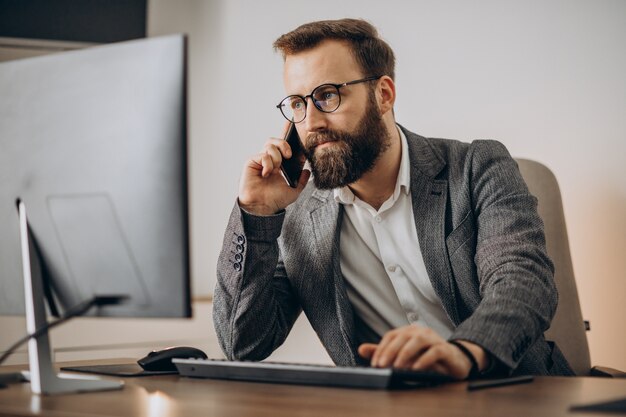 Jeune homme d'affaires parlant au téléphone et travaillant sur ordinateur