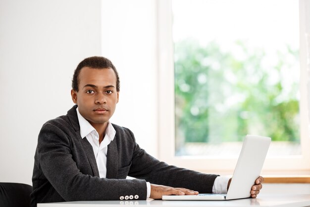 Jeune homme d'affaires prospère, assis sur le lieu de travail avec ordinateur portable