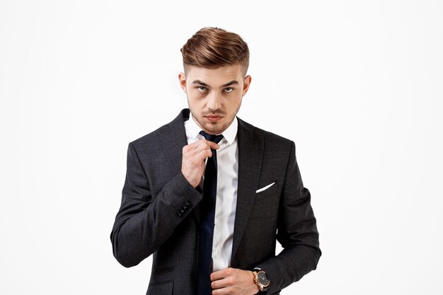 Jeune homme d'affaires prospère en costume corrigeant la cravate.