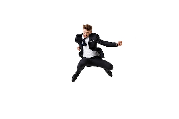 Jeune homme d'affaires prospère en costume se réjouissant de sauter sur fond blanc