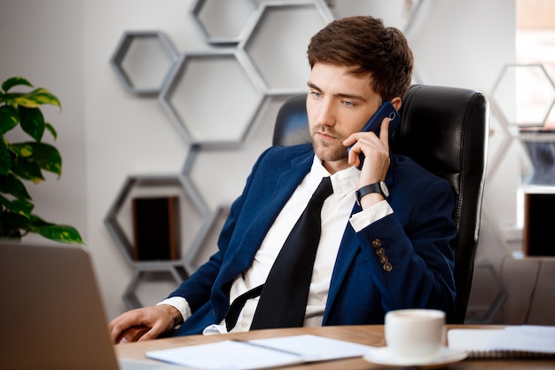 Jeune homme d'affaires prospère, parlant au téléphone, fond de bureau.