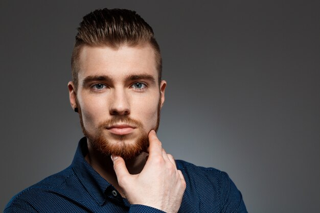 Jeune homme d'affaires prospère posant sur un mur sombre.