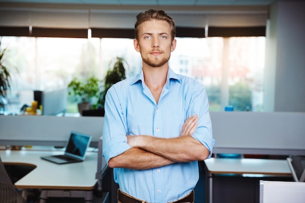 Photo gratuite jeune homme d'affaires prospère souriant, posant avec les bras croisés, sur le bureau