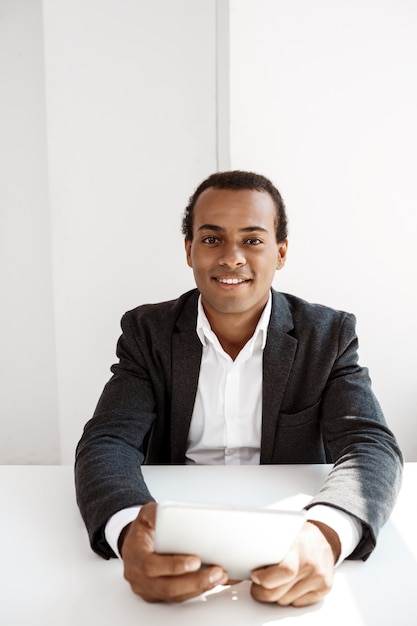Photo gratuite jeune homme d'affaires prospère, souriant, tenant la tablette, assis sur le lieu de travail