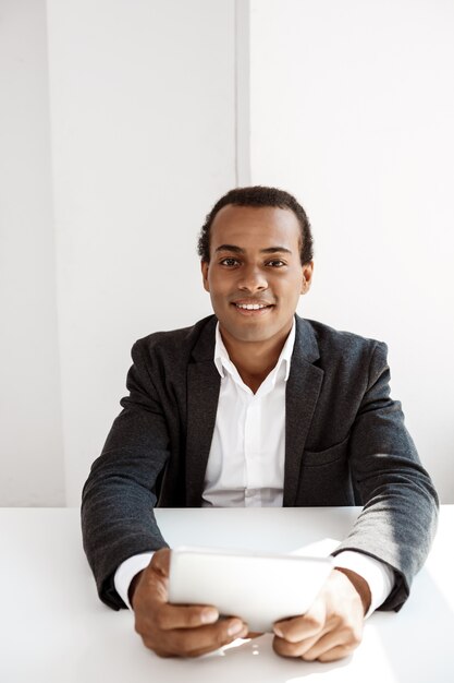 Jeune homme d'affaires prospère, souriant, tenant la tablette, assis sur le lieu de travail