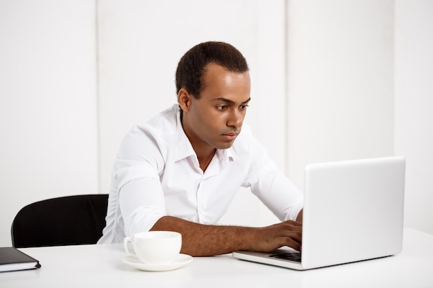 Photo gratuite jeune homme d'affaires prospère, tapant sur un ordinateur portable, assis au lieu de travail