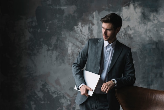 Jeune homme d&#39;affaires se penchant sur une chaise tenant un ordinateur portable à la main sur fond grunge