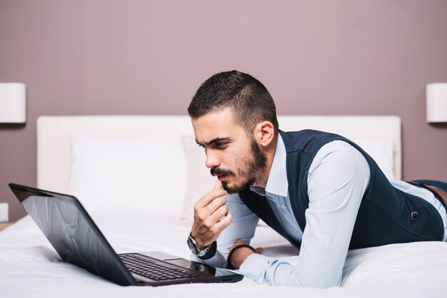 Jeune homme d&#39;affaires songeur avec ordinateur portable sur le lit