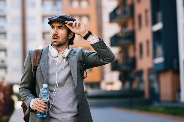 Jeune homme d'affaires transportant une bouteille d'eau en se promenant dans la ville et en détournant les yeux.