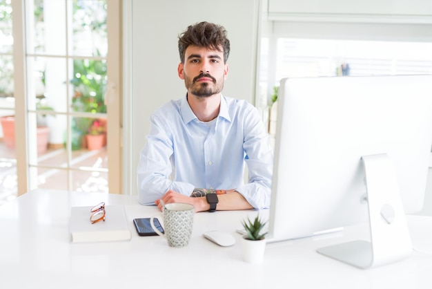 Photo gratuite jeune homme d'affaires travaillant à l'aide d'un ordinateur avec une expression sérieuse sur le visage simple et naturel regardant la caméra