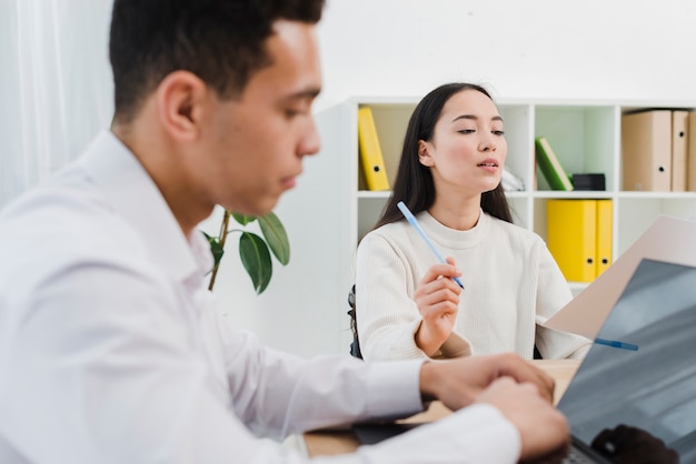 Jeune homme d&#39;affaires utilisant un ordinateur portable et son collègue lisant le document au bureau