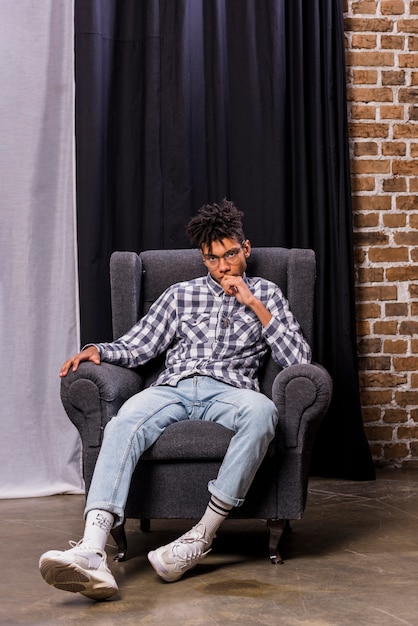 Jeune homme africain assis sur une chaise devant le rideau en regardant la caméra
