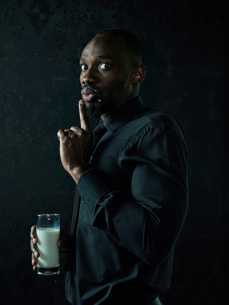 Jeune homme africain en bonne santé tenant une tasse de lait sur un studio bllack.