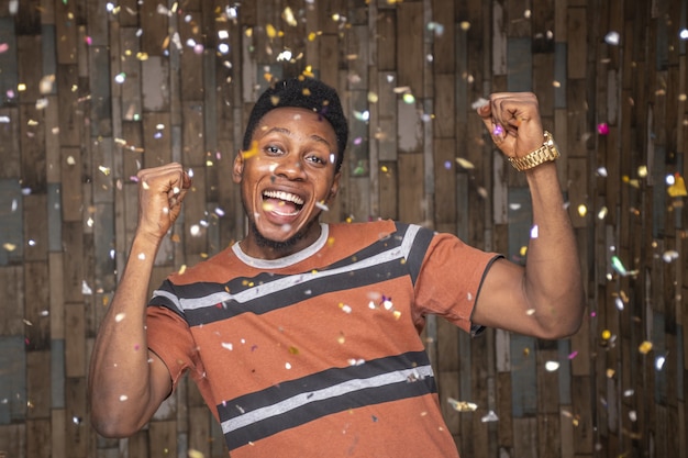 Photo gratuite jeune homme africain célébrant avec des confettis flottant autour