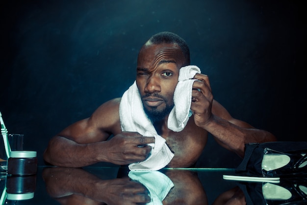 Le Jeune Homme Africain Dans La Chambre Assis Devant Le Miroir Après S'être Gratté La Barbe à La Maison. Concept D'émotions Humaines