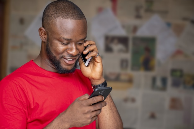 Jeune homme africain parlant au téléphone tout en utilisant un autre dans une pièce