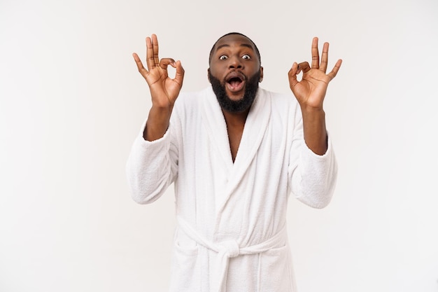 Jeune homme africain en peignoir se préparer aux soins de la peau montrant le signe du doigt ok Concept d'émotions humaines