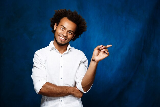 Jeune homme africain, pointant le doigt sur le côté sur le mur bleu.