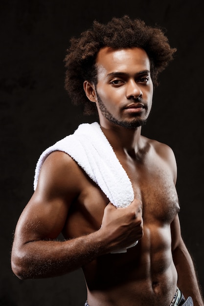 Photo gratuite jeune homme africain sportif posant sur le mur noir.