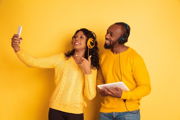 Jeune homme afro-américain émotionnel et femme dans des vêtements décontractés lumineux sur l'espace jaune. Beau couple