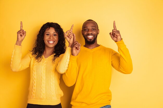 Jeune homme afro-américain émotionnel et femme en vêtements décontractés lumineux posant sur l'espace jaune. Beau couple