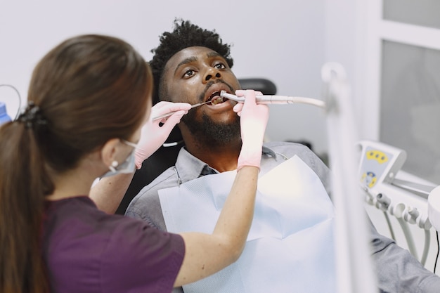 Photo gratuite jeune homme afro-américain. guy visitant le cabinet du dentiste pour la prévention de la cavité buccale. homme et médecin de famille pendant le contrôle des dents.